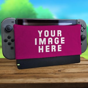 Puede incluir: Una funda de tela rosa con el texto "YOUR IMAGE HERE" impreso en ella. La funda está unida a una consola Nintendo Switch negra.