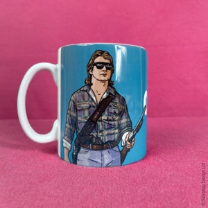 May include: A white ceramic mug with a blue background featuring a cartoon illustration of a man wearing a plaid shirt, sunglasses with the word "OBEY" printed on the lenses, and a gun. The man is holding a shotgun in his right hand.