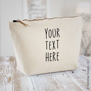 Könnte beinhalten: Eine beige Canvas-Kosmetiktasche mit dem Aufdruck "YOUR TEXT HERE" in Schwarz.