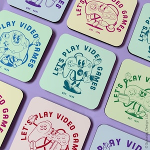 May include: Set of six square coasters with a retro video game theme. Each coaster features a different coloured background with a cartoon video game controller and the text "Let's Play Video Games" with an established year.