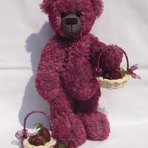 May include: A plush purple teddy bear holding a small wicker basket filled with red raspberries. The bear is standing on a white surface.