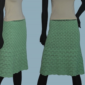 May include: A sleeveless, light beige top with a multi-colored necklace and a green crocheted skirt.
