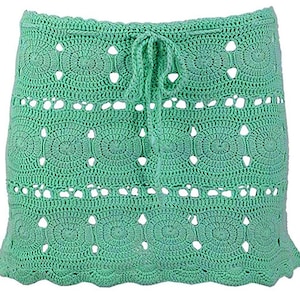 May include: A green crochet skirt with a tie at the waist. The skirt has a scalloped hem and a circular pattern.