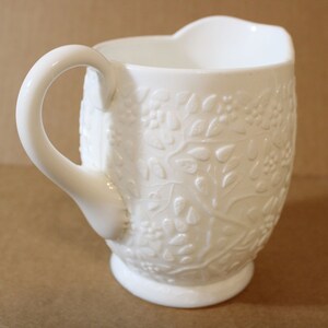 Jarra de crema blanca con hojas grandes en relieve, enredaderas y flores