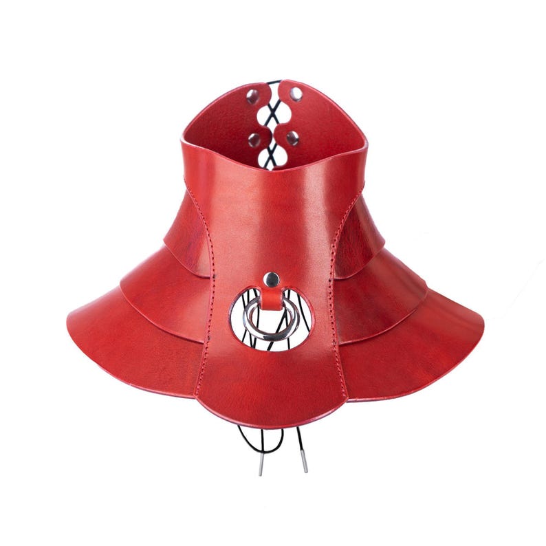May include: A red leather choker necklace featuring a multi-layered, flared collar design. The piece includes a central silver-toned metal ring, visible stitching along the edges, and a black lace-up closure with metal eyelets at the back.