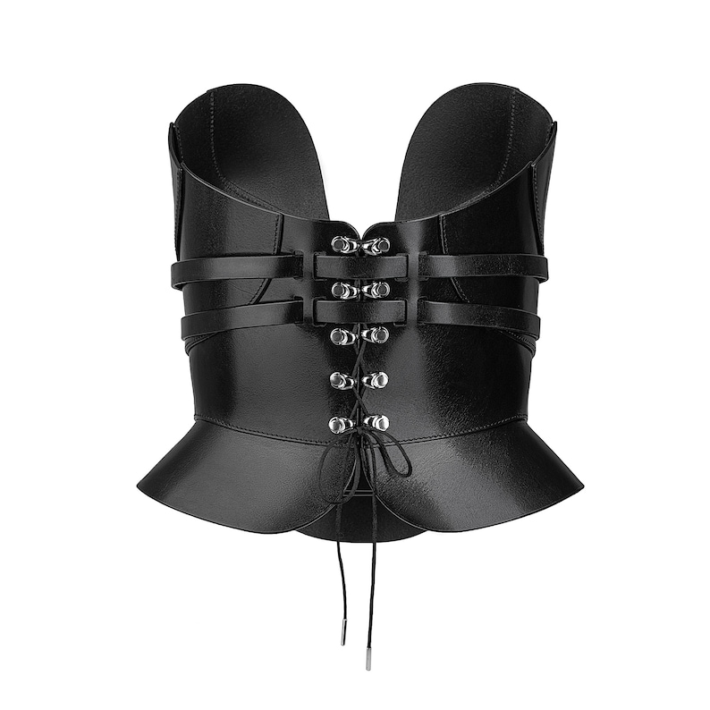 May include: A black corset top featuring a structured bodice with a deep U-shaped neckline. The garment includes horizontal straps across the front, silver-toned metal eyelets, and a central lace-up closure with long black strings hanging below.