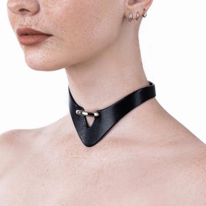 Può includere: Un choker in pelle nera con un dettaglio ad anello argentato. Il choker ha un design a V ed è regolabile.