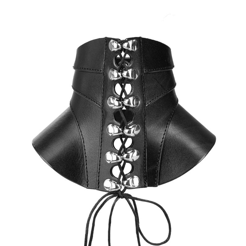 May include: A black corset belt featuring a structured design with vertical panels. The front center includes a black lace-up closure threaded through silver-toned metal eyelets, with long black laces hanging from the bottom edge of the garment.