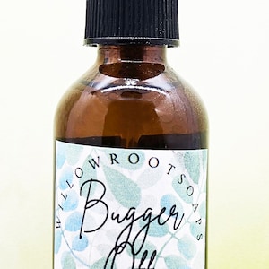 May include: A brown glass spray bottle labeled "Bugger Off" with a black cap and clear sprayer. The label features a blue and green leaf pattern and the words "Willow Root Soaps". The bottle is filled with a clear liquid.
