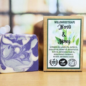 May include: A rectangular bar of soap with a purple and white marbled pattern next to a brown cardboard box. The label reads Willowrootsoaps Neroli & Honey, listing ingredients like apricot oil, cocoa butter, and coconut oil, with vegan and cruelty-free icons.