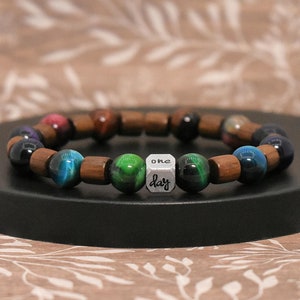 May include: A beaded bracelet with brown wooden beads, tiger's eye beads in shades of green, blue, and gold, and a silver charm that says "one day".