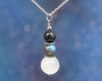 May include: A silver chain necklace with a three-tiered pendant featuring black, blue, and white gemstone beads.