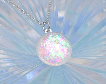 May include: A silver chain necklace with a iridescent white pearl pendant. The pearl has a glittery finish.