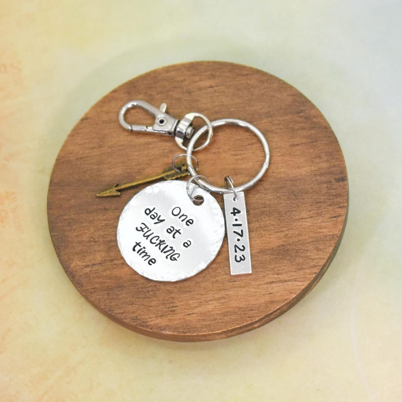 Peut inclure: Porte-cl&eacute;s en argent avec un charme rond qui dit "One day at a time" et une &eacute;tiquette en argent avec la date "4-17-23".