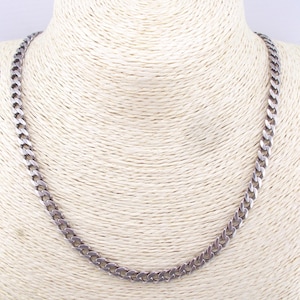Op de afbeelding: Een zilverkleurige metalen ketting met een klassiek gourmet schakelontwerp. De ketting bestaat uit uniforme, in elkaar grijpende ovale schakels met een gepolijste afwerking, waardoor een doorlopende, flexibele lus rond de nek ontstaat.