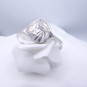 Op de afbeelding: Een zilveren ring met een uniek, abstract ontwerp. De ring ligt op een witte achtergrond.