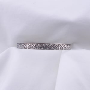 May include: A silver bangle bracelet with a decorative wave pattern.