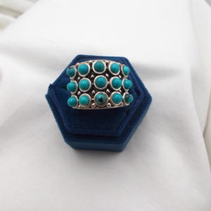 Peut inclure: Une large bague en argent ornée de trois rangées horizontales de petits cabochons de turquoise ronds et polis. Les pierres turquoise sont serties dans des chatons en argent individuels avec de petites perles d'argent entre chaque pierre.