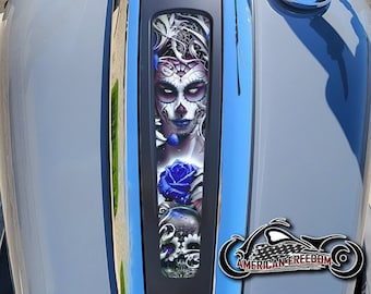 May include: A blue and gray motorcycle gas tank with a black decal featuring a woman with a sugar skull face and a blue rose. The decal also includes the text "Road Glide" and "American Freedom".