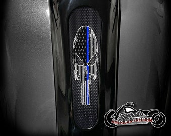 Puede incluir: Un gráfico de calavera en blanco y negro con una bandera estadounidense y una línea azul, que representa la línea azul fina, en una cubierta de tanque de motocicleta negra.