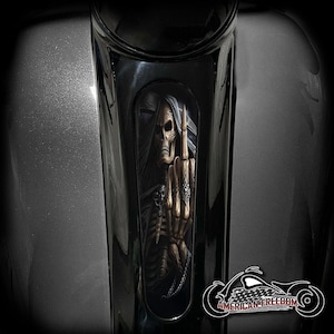 May include: A black motorcycle fuel tank with a skeleton hand giving the middle finger in a black and white graphic. The graphic is in a rectangular shape and is on the side of the tank. The text "AMERICAN FREEDOM" is on the bottom of the image.