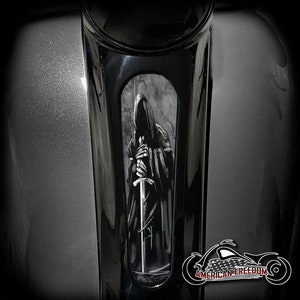 May include: Black and white graphic of a hooded figure holding a sword, printed on a motorcycle gas tank. The graphic is in a vertical rectangular shape.