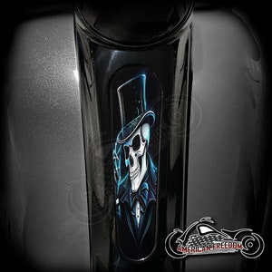 Könnte beinhalten: Ein schwarzer und blauer Schädel, der einen Zylinder und eine Fliege trägt. Der Schädel ist in einem schwarzen Anzug und hat einen blauen Schein um sich herum. Das Bild ist auf einem schwarzen Motorrad-Benzintank.