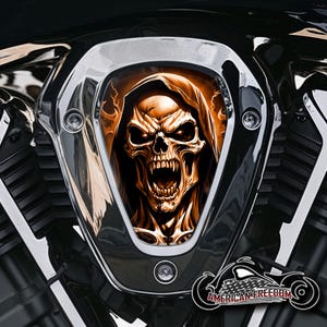 Könnte beinhalten: Ein verchromter Motorrad-Lufteinlassdeckel mit einer Totenkopfgrafik. Der Totenkopf trägt eine Kapuze und ist von Flammen umgeben. Der Totenkopf ist orange und schwarz, und die Flammen sind orange und gelb.