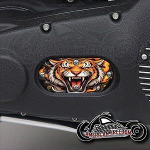 Puede incluir: Una cubierta de motor de motocicleta negra con una pegatina redonda de un rostro de tigre naranja y negro. La pegatina tiene un fondo blanco y la boca del tigre está abierta, mostrando dientes afilados.