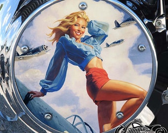 May include: A round metal cover with a pin-up girl illustration and three vintage airplanes. The girl is wearing a blue shirt and red shorts. The background is a blue sky with white clouds.