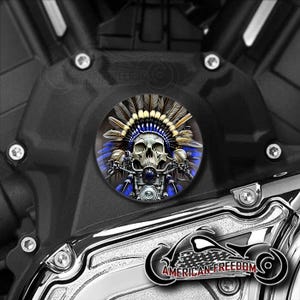 May include: A black motorcycle engine with a chrome cover. A round sticker featuring a skull wearing a blue and white headdress is on the cover. The sticker has the words "American Freedom" on it.