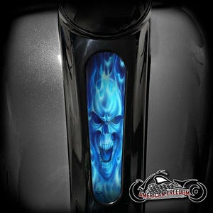 May include: A motorcycle part with a black finish and a blue flame skull design. The skull has an open mouth and is surrounded by blue flames. The American Freedom logo is visible on the lower right.