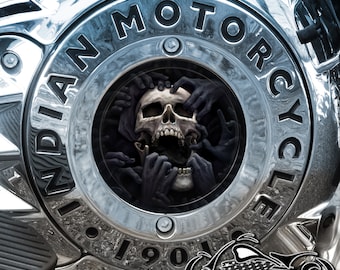 May include: A chrome motorcycle engine cover with a black skull and hands graphic. The cover has the words "INDIAN MOTORCYCLE" and "1901" inscribed on it.