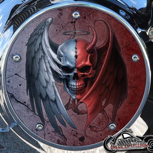 Puede incluir: Una pieza de motocicleta con un gráfico detallado de una calavera dividida, mitad ángel y mitad diablo, con alas y cuernos. El diseño está en tonos de gris, rojo y blanco, sobre un fondo texturizado. El logotipo "AMERICAN FREEDOM" está en la parte inferior.