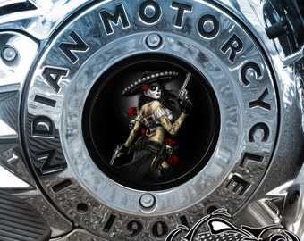 May include: A silver motorcycle engine cover with the words "INDIAN MOTORCYCLE" and "1901" inscribed around a circular opening. The opening features a black and white image of a woman wearing a sombrero and holding a gun, with red roses in the background.