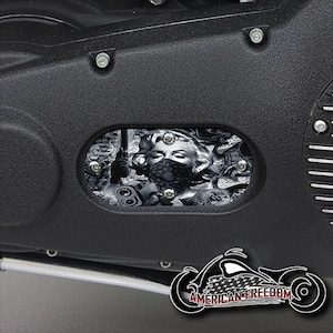 May include: Black and white motorcycle engine cover with a graphic of a woman wearing a bandana and holding a gun. The graphic is in a rectangular shape and is surrounded by a black border.