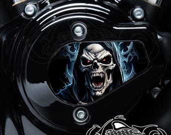 Puede incluir: Tapa de motor de motocicleta negra con un gráfico de calavera. La calavera lleva una túnica con capucha y tiene ojos rojos brillantes. El gráfico está rodeado por un diseño de llamas azules y blancas.