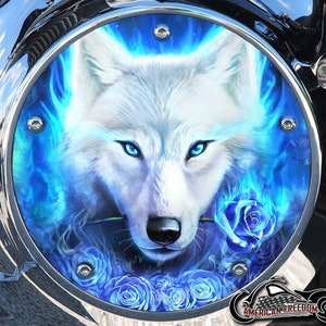 Puede incluir: Un lobo blanco con ojos azules está rodeado de rosas azules y llamas azules. La imagen está en una tapa de gasolina de motocicleta redonda y plateada.