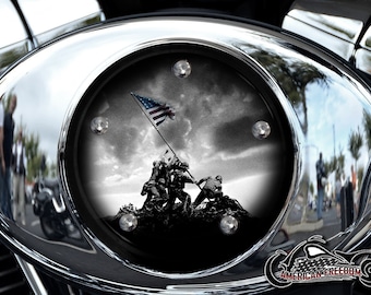 May include: A chrome motorcycle emblem with a black and white image of the iconic Iwo Jima flag raising scene. The image is surrounded by a silver ring with five silver studs. The text "AMERICAN FREEDOM" is printed below the image.