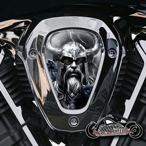 Könnte beinhalten: Ein schwarzer und silberner Motorrad-Lufteinlassdeckel mit einer Grafik eines Wikingerkriegers mit Bart und einem gehörnten Helm. Der Krieger ist von Raben und Blitzen umgeben.