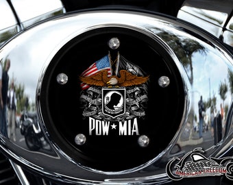 May include: A black motorcycle engine cover with a POW MIA emblem. The emblem features an American flag, a bald eagle, and a soldier's silhouette. The text "Some Gave Some All" is written on a banner.