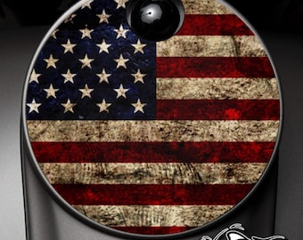 May include: A round, metallic object featuring a distressed American flag design in red, white, and blue. The design includes stars and stripes, with a black, circular element at the top. The words "AMERICAN FREEDOM" are displayed below the flag.