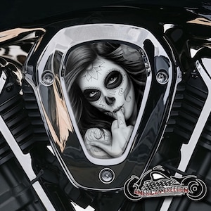 Könnte beinhalten: Ein verchromter Motorradmotordeckel mit einem Schwarz-Weiß-Bild einer Frau mit Sugar-Skull-Make-up. Die Frau berührt ihre Lippen mit dem Finger. Der Text "AMERICAN FREEDOM" ist zu sehen.