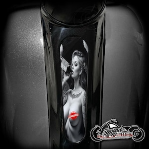 May include: A motorcycle part with a black and white graphic of a woman drinking from a bottle. The image is partially censored with a red circle. The words "American Freedom" are displayed with a motorcycle graphic.
