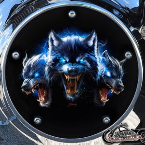 Puede incluir: Una cubierta de motocicleta negra con un borde cromado y un gráfico de tres lobos con ojos azules y rayos. Los lobos están gruñendo y tienen dientes afilados. El texto "American Freedom" está en la parte inferior de la imagen.