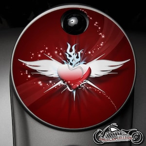 May include: A red gas cap with a white winged heart and a blue flame design. The heart has a red and white gradient. The background is red with white sparkles.