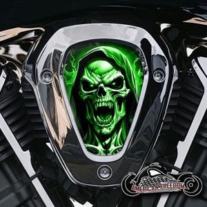 Könnte beinhalten: Ein Motorradmotorkomponente mit einem Chromrahmen. Das zentrale Design zeigt einen leuchtend grünen Schädel mit Kapuze und einem bedrohlichen Ausdruck. Der Text "AMERICAN FREEDOM" ist auf einem Logo unten sichtbar.