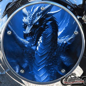 May include: A blue dragon graphic is featured on a motorcycle part. The dragon is detailed with scales and horns, set against a blue background. The part is framed by a chrome border and secured with silver bolts. The American Freedom logo is visible.
