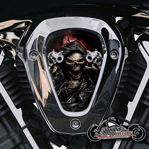 Könnte beinhalten: Ein schwarzer und verchromter Motorradluftfilter mit einer Grafik eines Skeletts, das einen Kapuzenumhang trägt und zwei Pistolen hält. Die Grafik ist vor einem roten und schwarzen Hintergrund platziert. Der Text "AMERICAN FREEDOM" ist am unteren Rand des Bildes sichtbar.