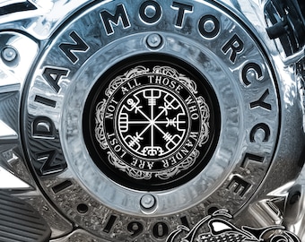 May include: A chrome motorcycle engine cover with a black circular sticker featuring a compass design and the text "Not all those who wander are lost". The sticker is surrounded by a decorative border. The engine cover has the words "Indian Motorcycle" and "1901" embossed on it.